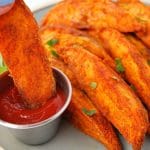 close up of a plate of sweet potato wedges with a wedge being dipped in ketchup