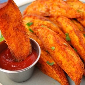 close up of a plate of sweet potato wedges with a wedge being dipped in ketchup