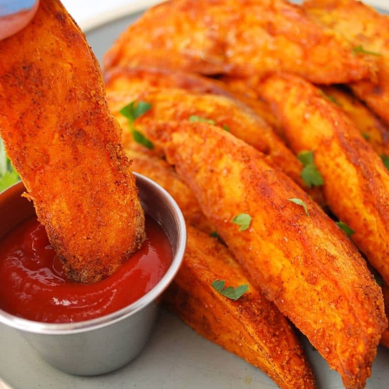 close up of a plate of sweet potato wedges with a wedge being dipped in ketchup