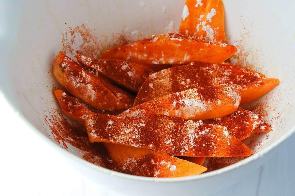 sweet potato wedges with seasoning ingredients ready to toss in a bowl