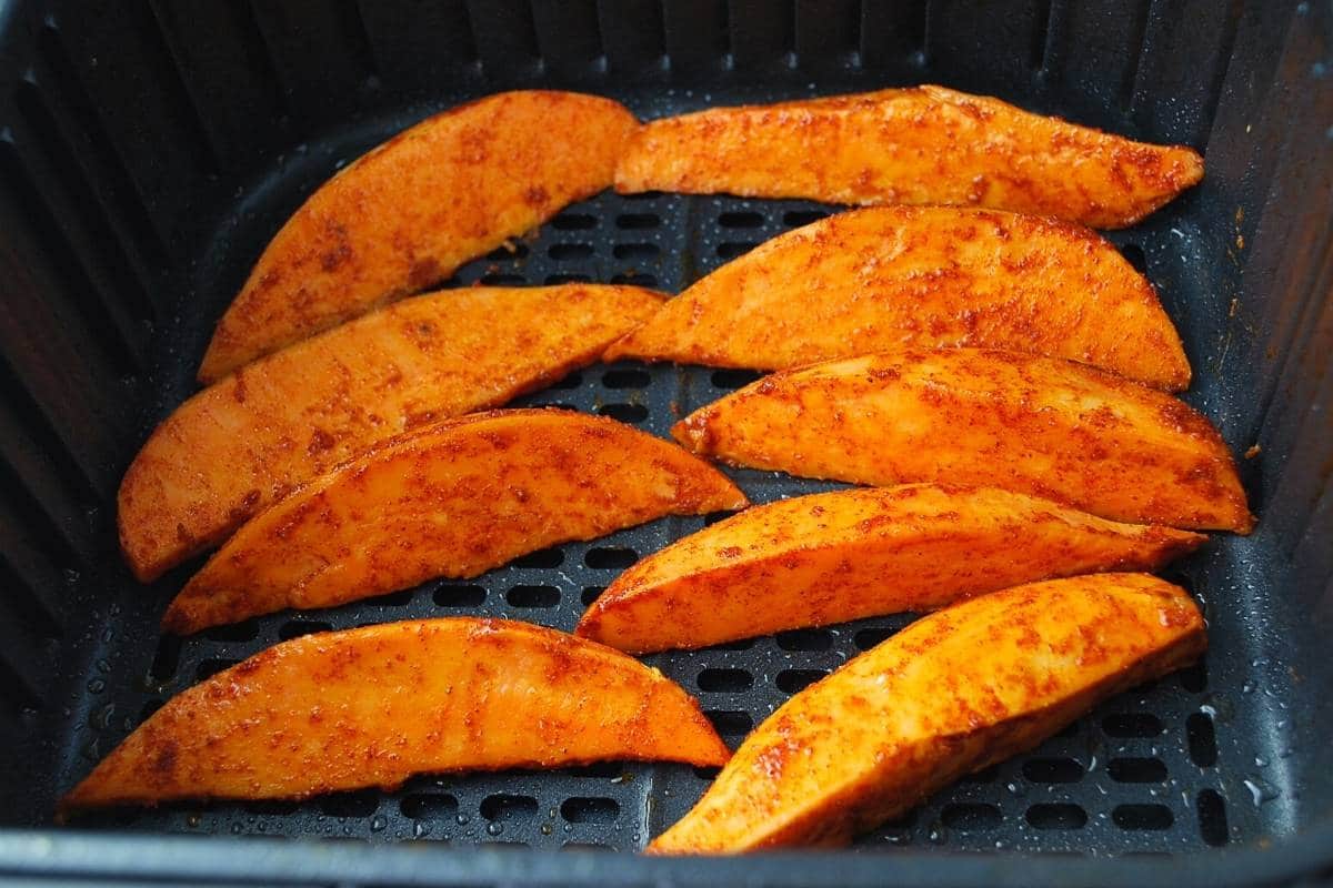 Seasoned sweet potato wedges in an air fryer basket ready to cook