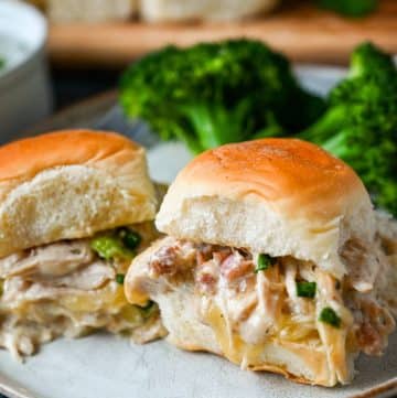 two Hawaiian rolls with shredded cheesy chicken with green onions inside on a plate with broccoli