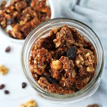 a glass jar filled with granola with nuts and raisins around it