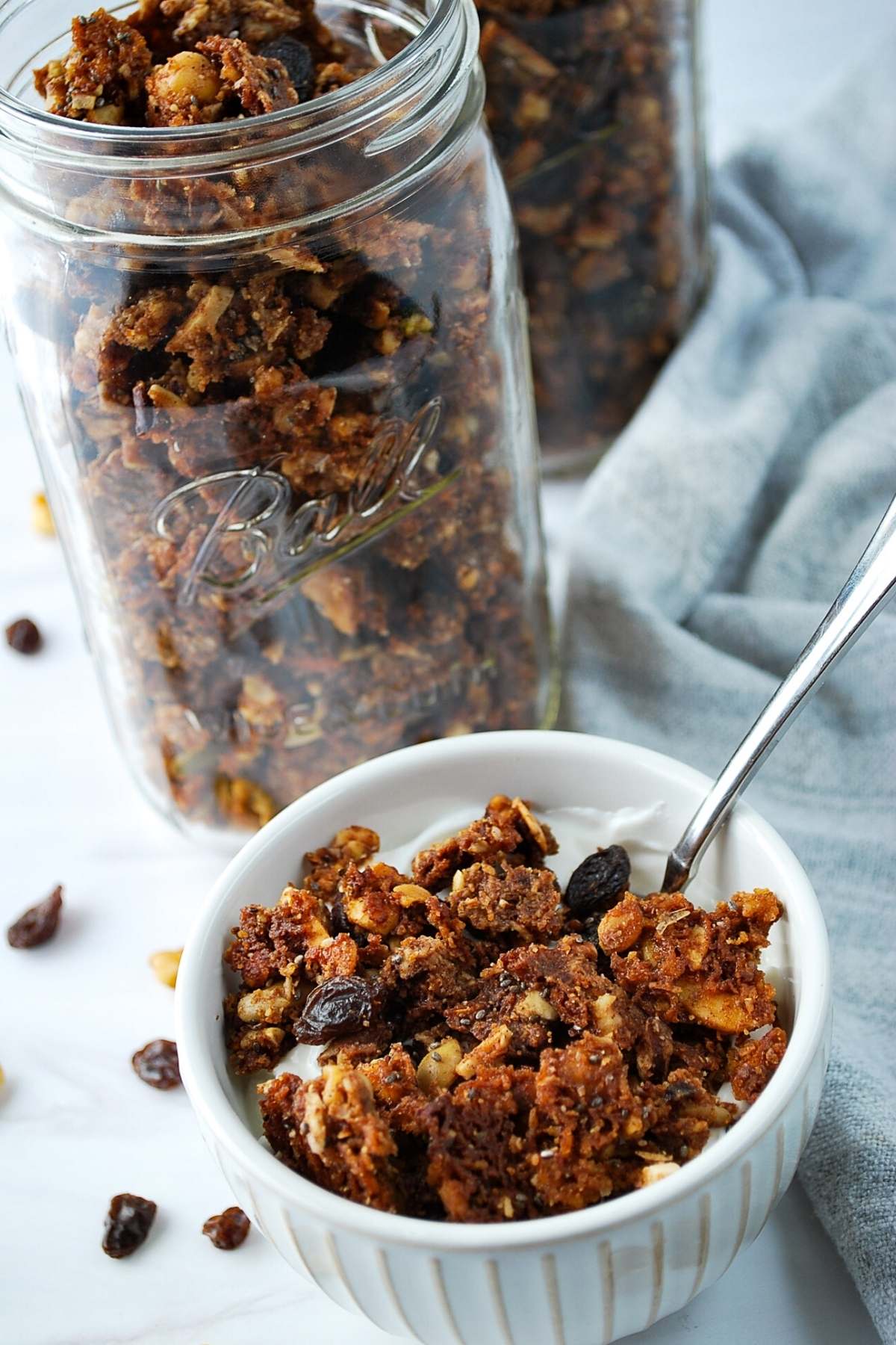 bowl of granola with a spoon with mason jars filled with granola in the background