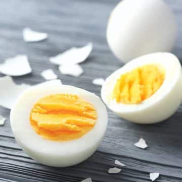 a perfectly cooked hard boiled egg sliced in half with a whole egg behind it