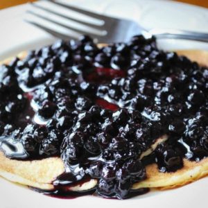 pancake topped with wild blueberry compote on a plate with a fork