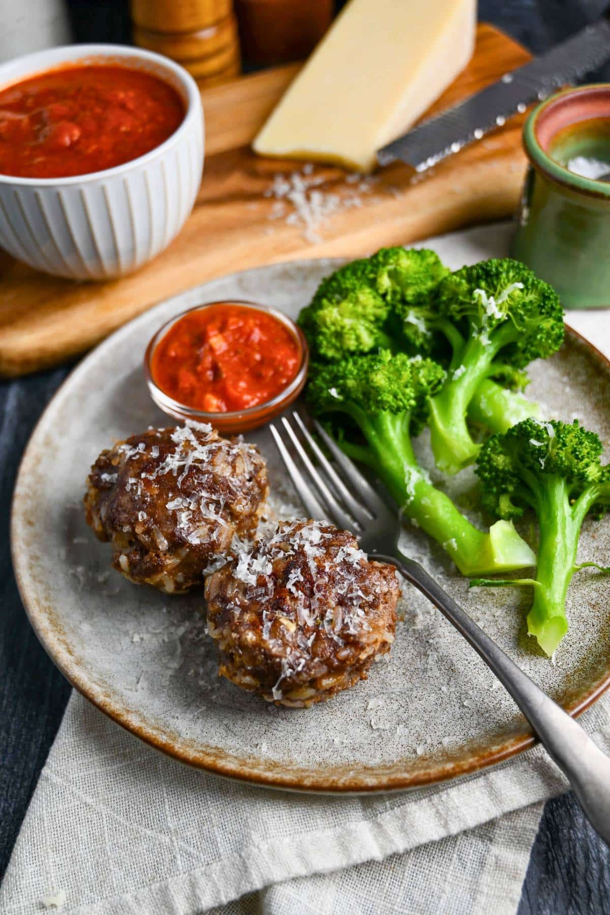 meatloaf muffins on a plate with broccoli and a dish of marinara topped with grated parmesan