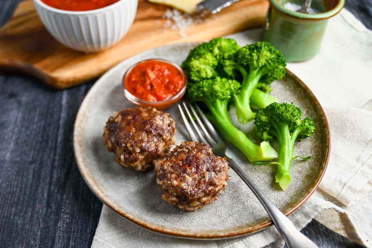 two gf mini meatloaves on a plate with steamed broccoli and a dish of marinara sauce
