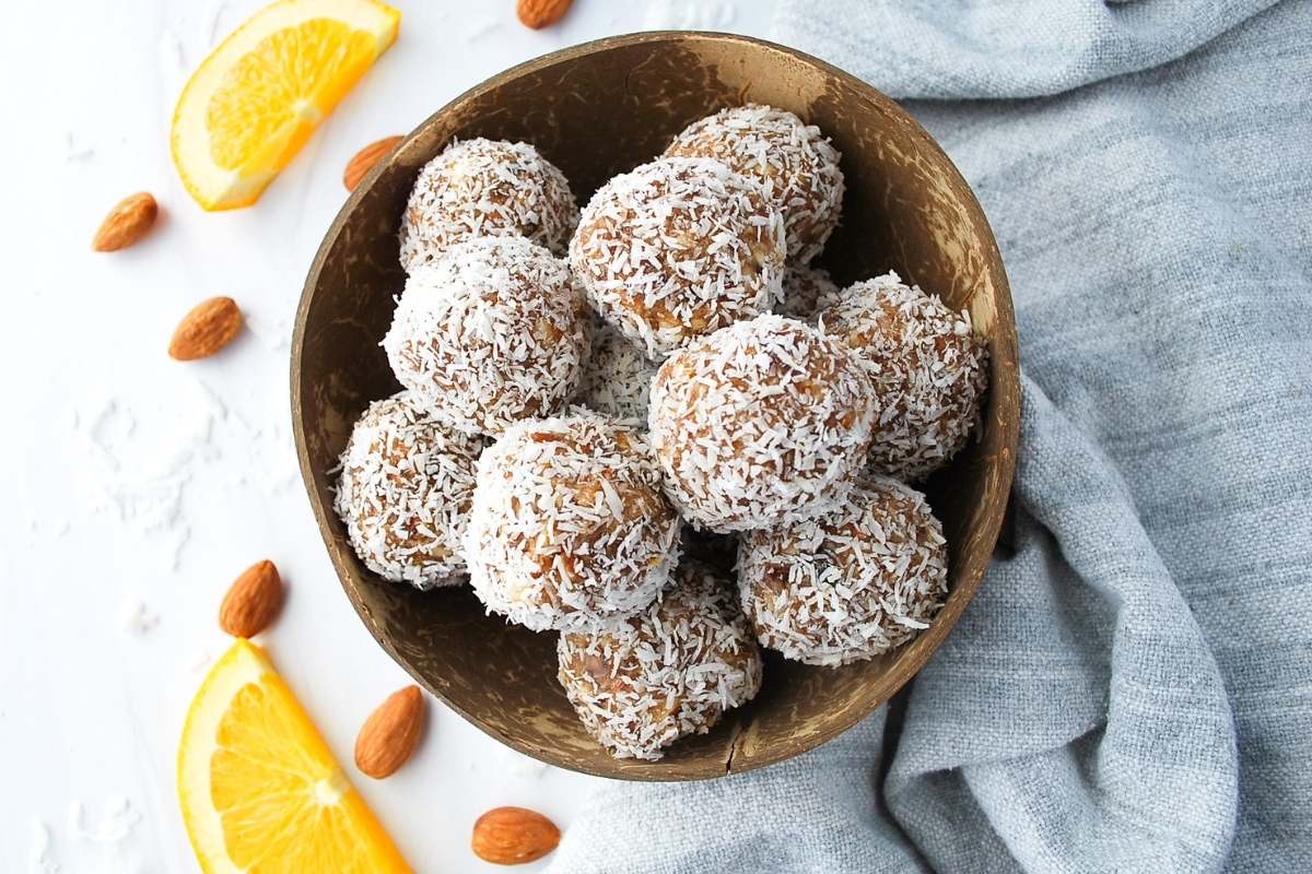 overhead photo of date balls in a coconut shell with slice orange and almonds around it