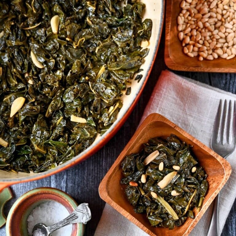 a pot of braised kale with garlic with a served portion and a bowl of toasted pine nuts