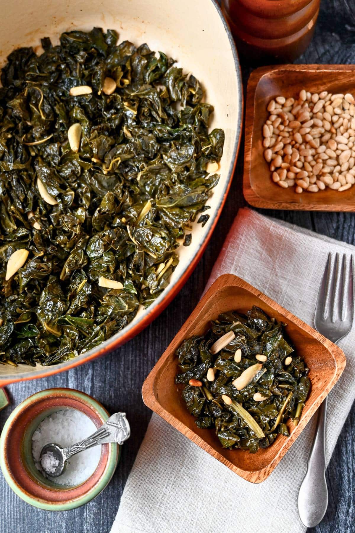 a dutch oven of braised kale and garlic with a wooden bowl next to it with a served portion