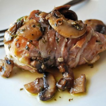close up of cooked chicken breast wrapped in prosciutto and topped with mushrooms