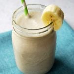overhead photo of a coconut banana smoothie in a glass with a straw and slice of banana