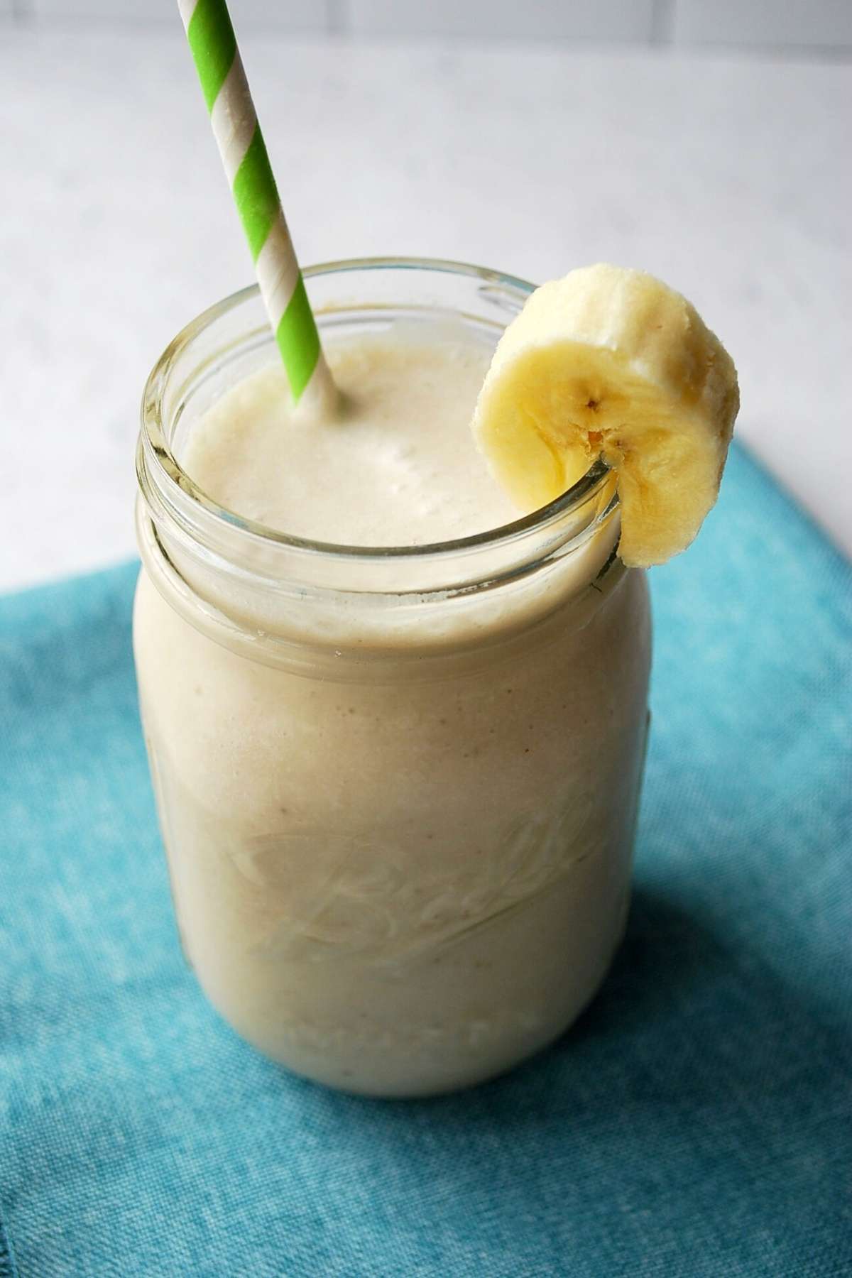 close up of a coconut banana smoothie in a mason jar with a slice of banana on the rim and a straw