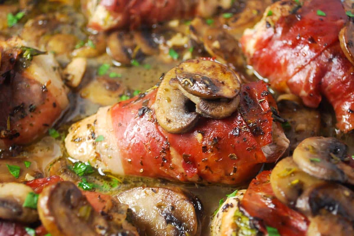 close up of a mushroom topped chicken breast in a pan wrapped in prosciutto ham