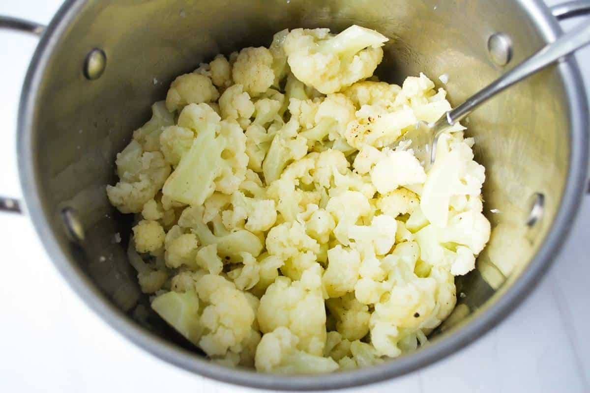 cauliflower florets in a pot with a fork