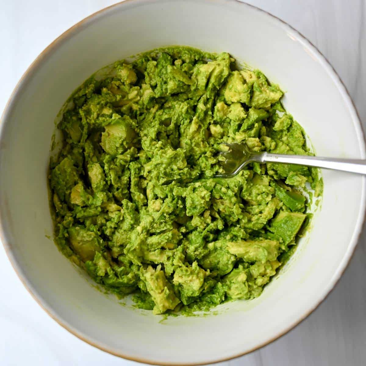 mashed avocado in a white bowl with a fork