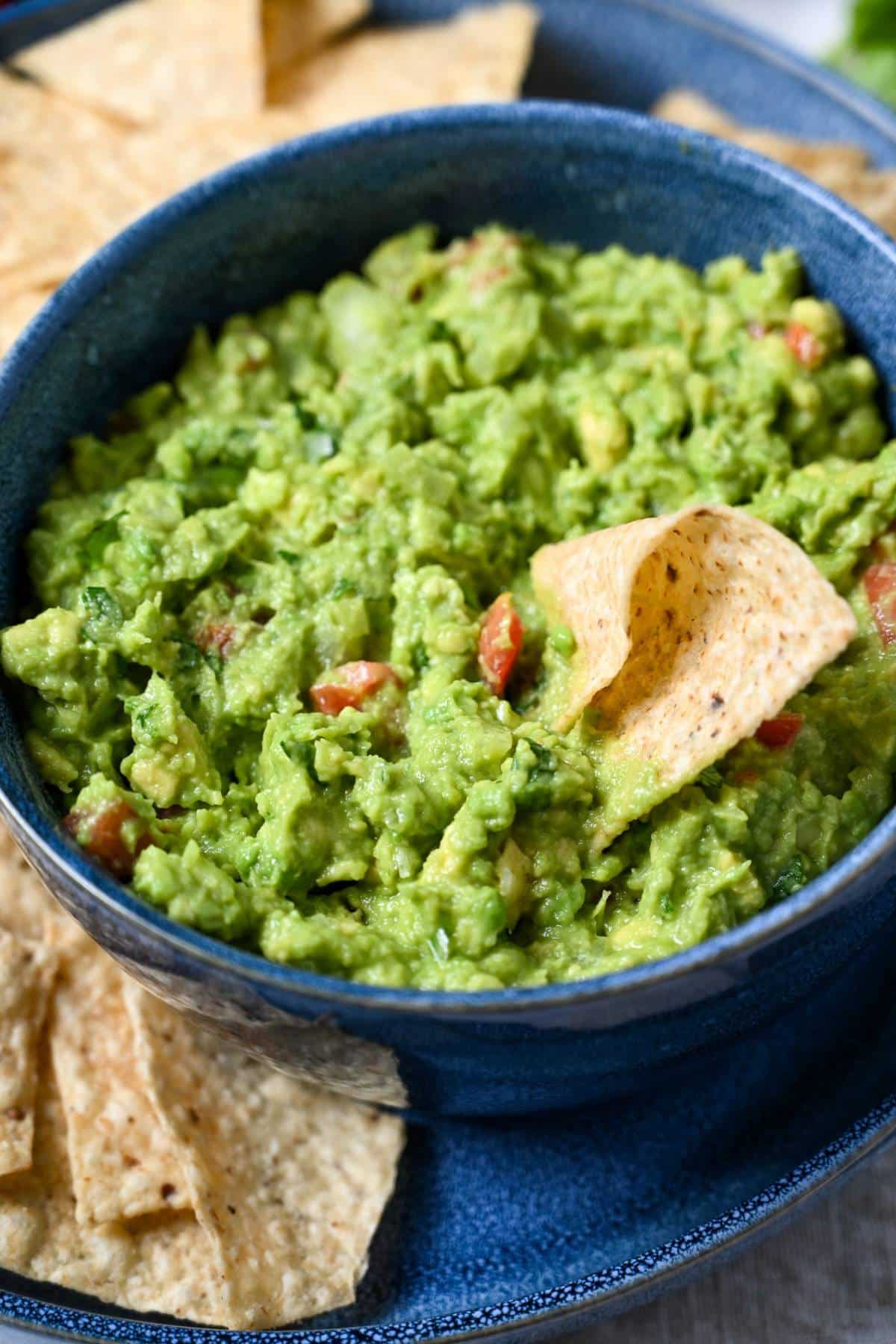 a chip dipped into a bowl of chunky guacamole with tortilla chips