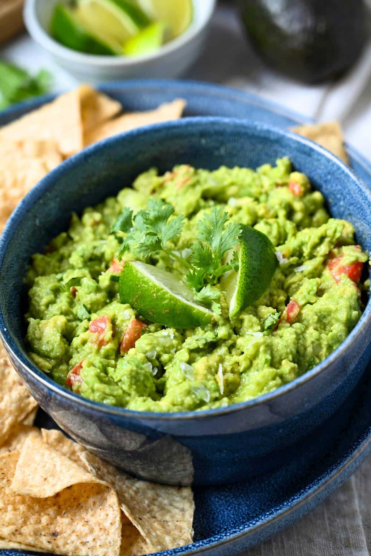 a bowl of guacamole with tortilla chips with two lime wedges and fresh cilantro on top