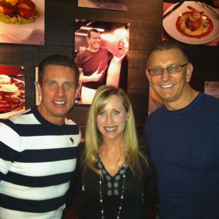 Two men and a woman smiling for the camera in a restaurant