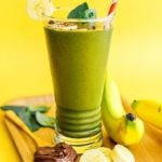 green smoothie in a glass with a bright yellow background