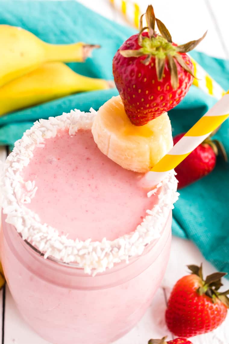 overhead photo of a strawberry smoothie with coconut on the rim and fresh fruit garnish