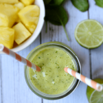 pineapple spinach smoothie in a glass with two straws and a bowl of pineapple in the background