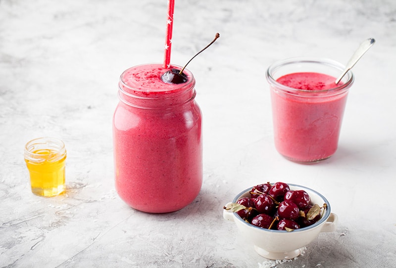 cherry pear spinach smoothie in a glass with cherries in a bowl in front