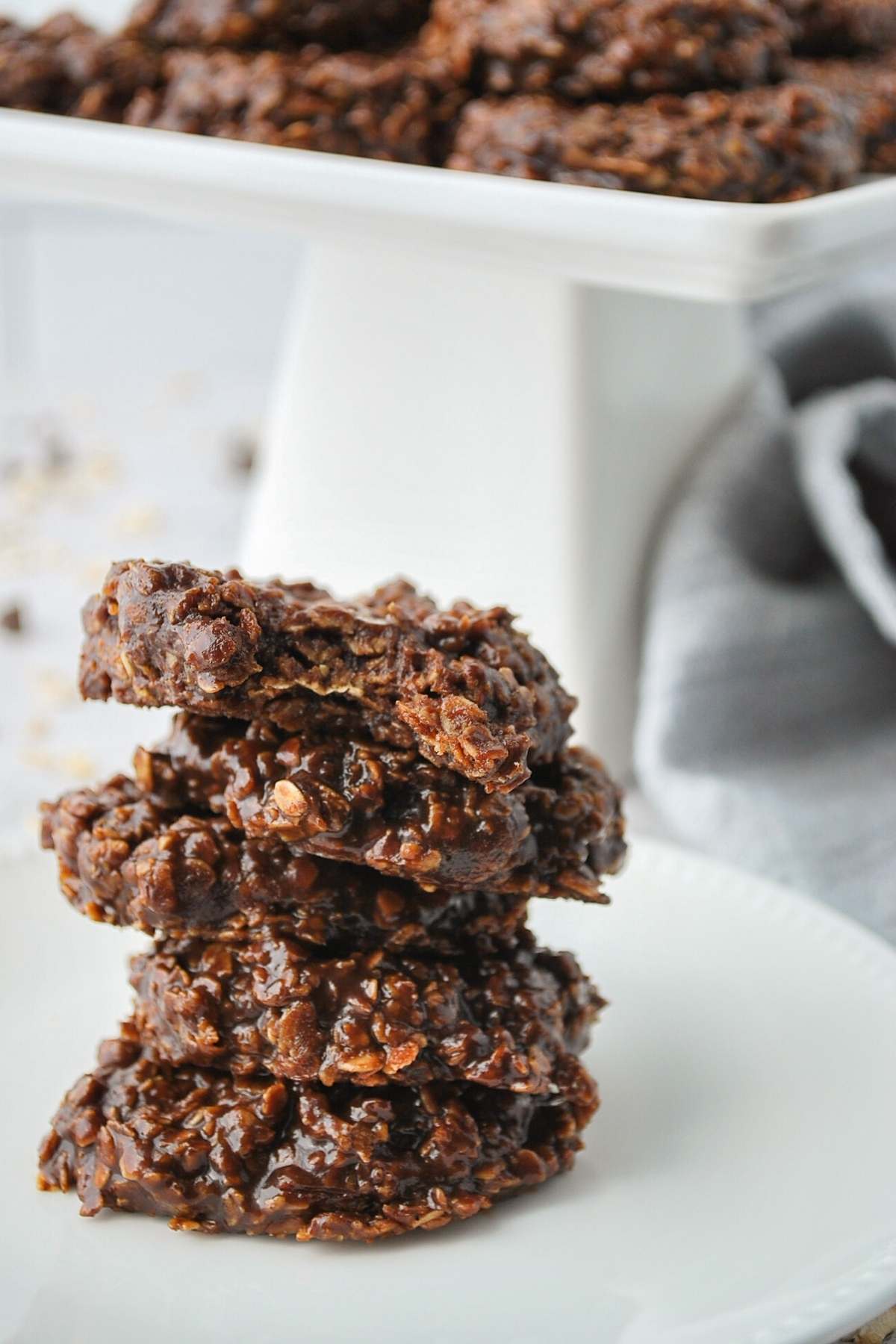 stacked dairy-free no-bake cookies on a white plate next to a white platter of no-bake cookies