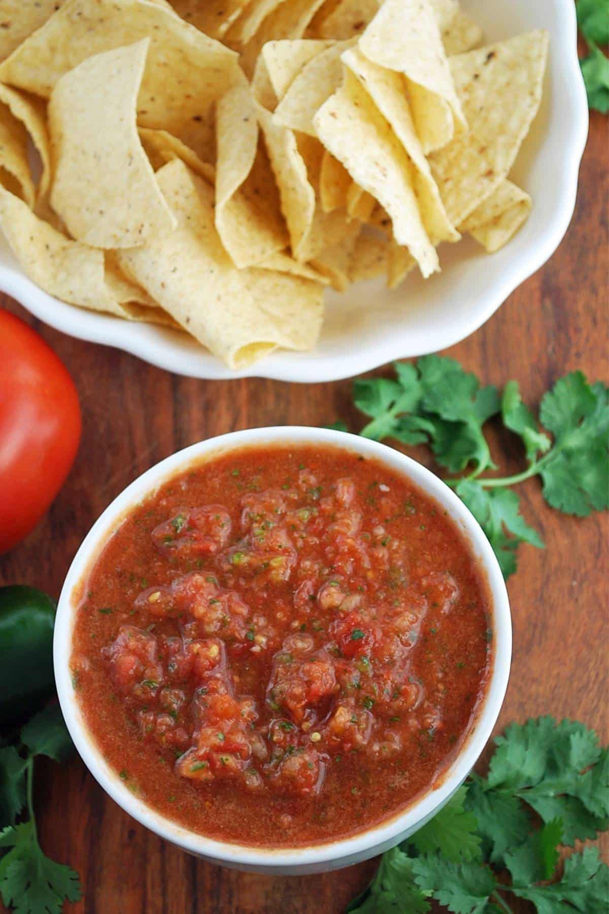 Overhead photo of a bowl of red salsa, cilantro and tortilla chips