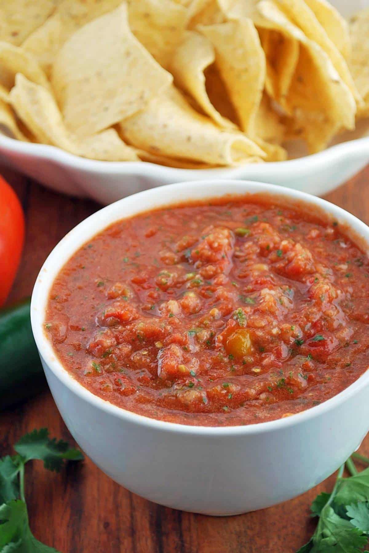 close up of a bowl of red tomato salsa made in a vitamix blender with a bowl of chips behind it