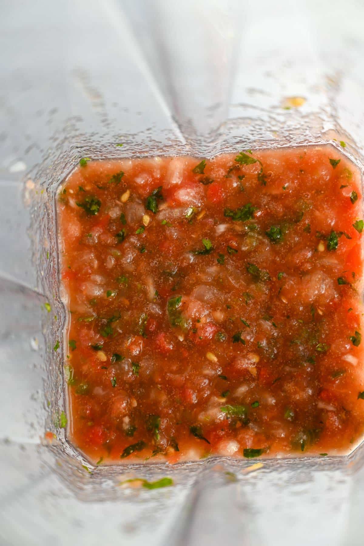 looking down into a blender canister of blended red tomato salsa