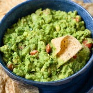 close up of a bowl of guacamole with a chip dipped in it