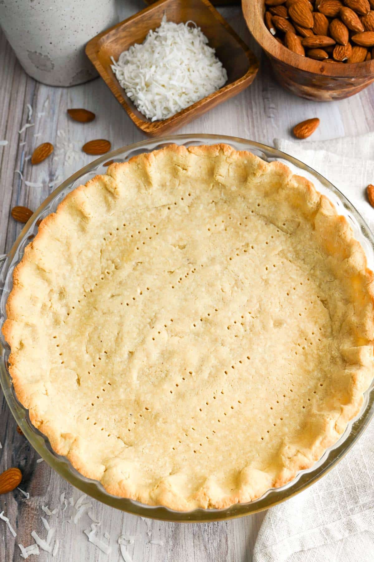 a baked almond pie crust with a bowl of coconut flakes and almonds