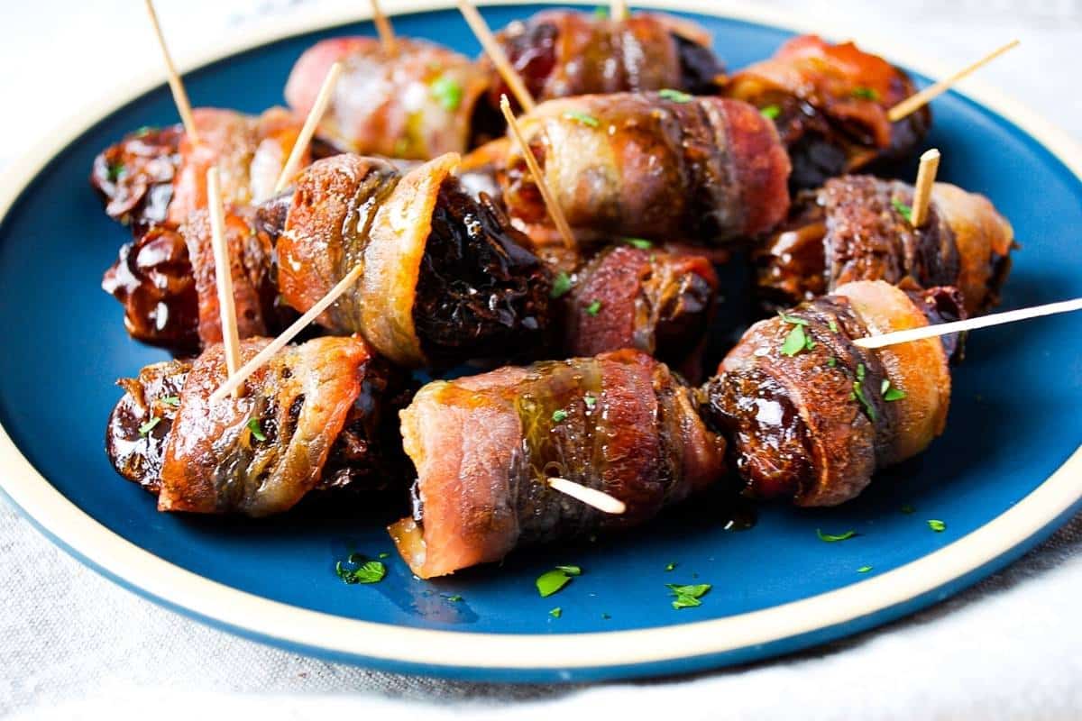 side view of maple drizzled stuffed dates with bacon on a plate with toothpicks for serving