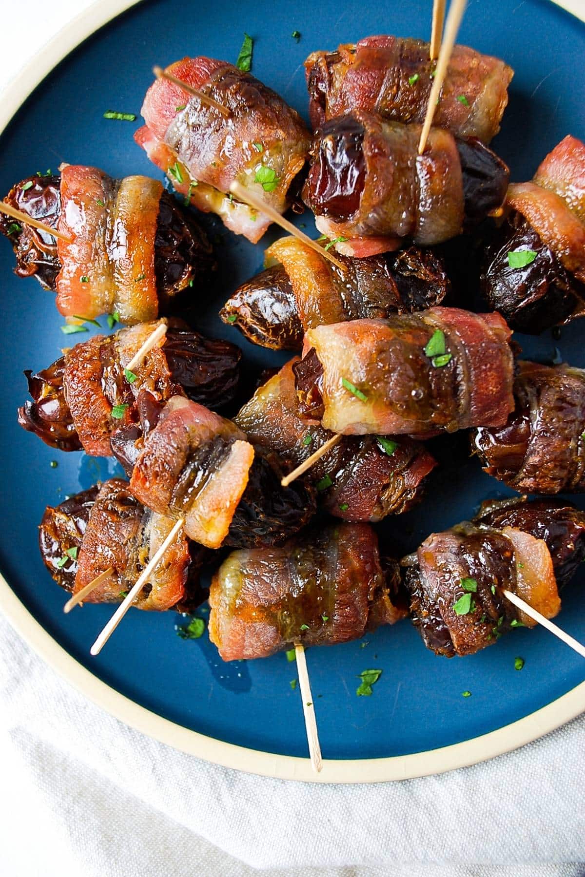 bacon wrapped dates on a blue plate drizzled with maple syrup