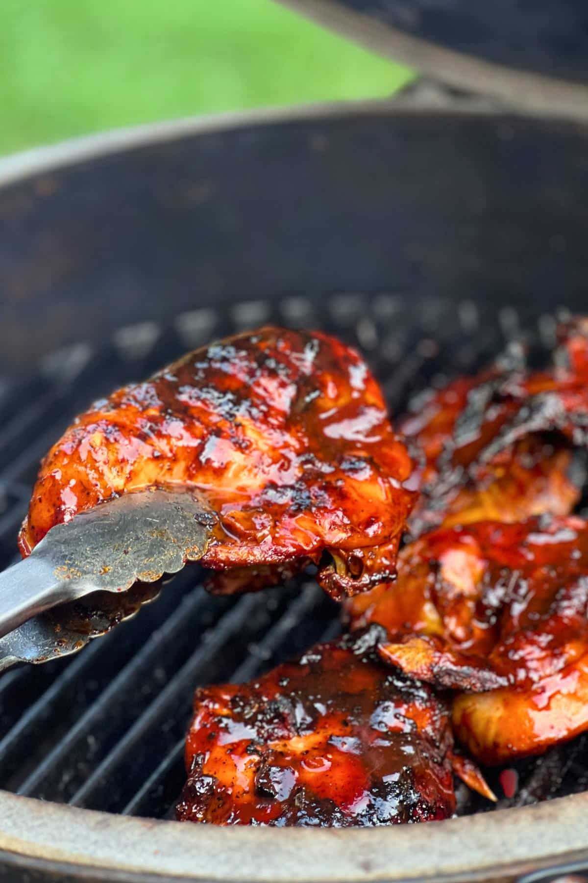 holding up a bone in bbq chicken breast on a big green egg with tongs