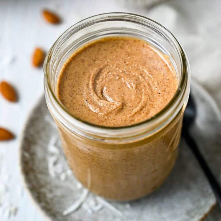 a jar of almond butter on a plate with coconut flakes and a spoon
