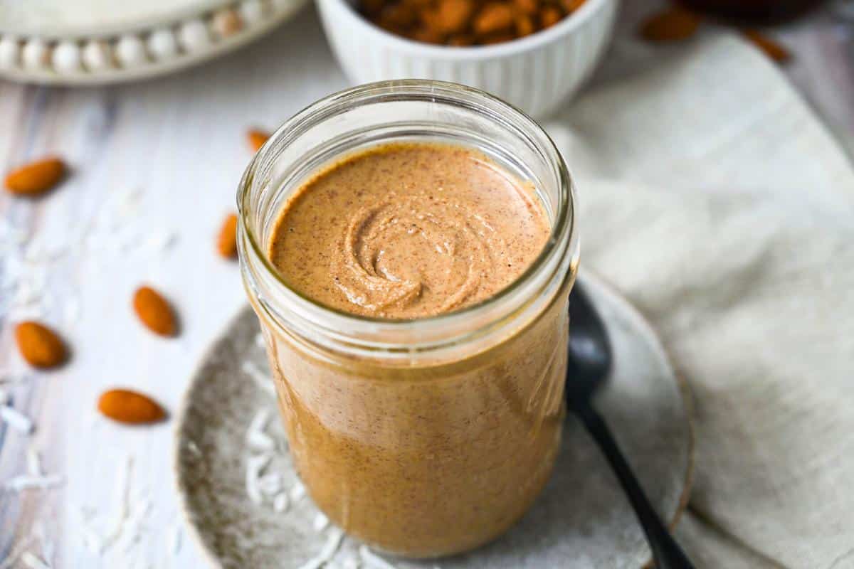 a jar of almond butter with whole almonds and coconut sprinkled around it