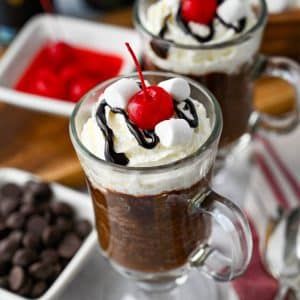 two hot cocoa mug cakes topped with whipped cream, chocolate sauce, marshmallows and a cherry