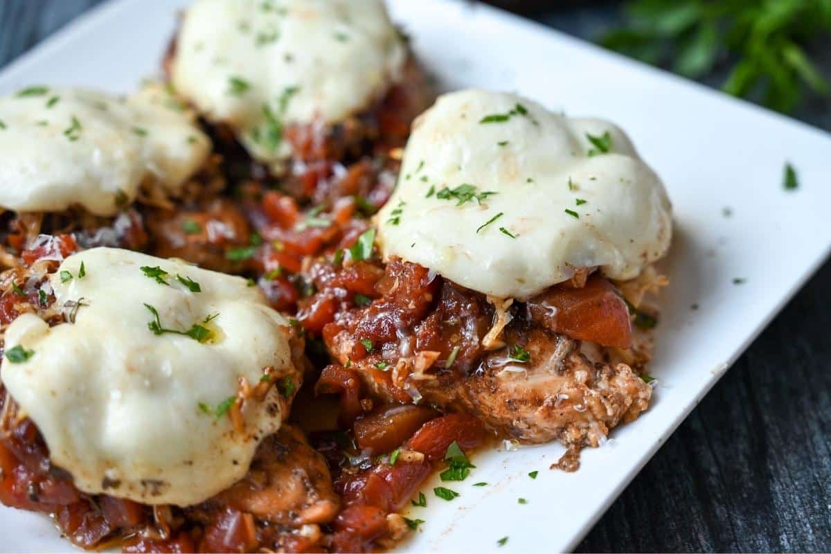 four chicken breasts topped with tomatoes, buffalo mozzarella, and chopped fresh basil on a plate