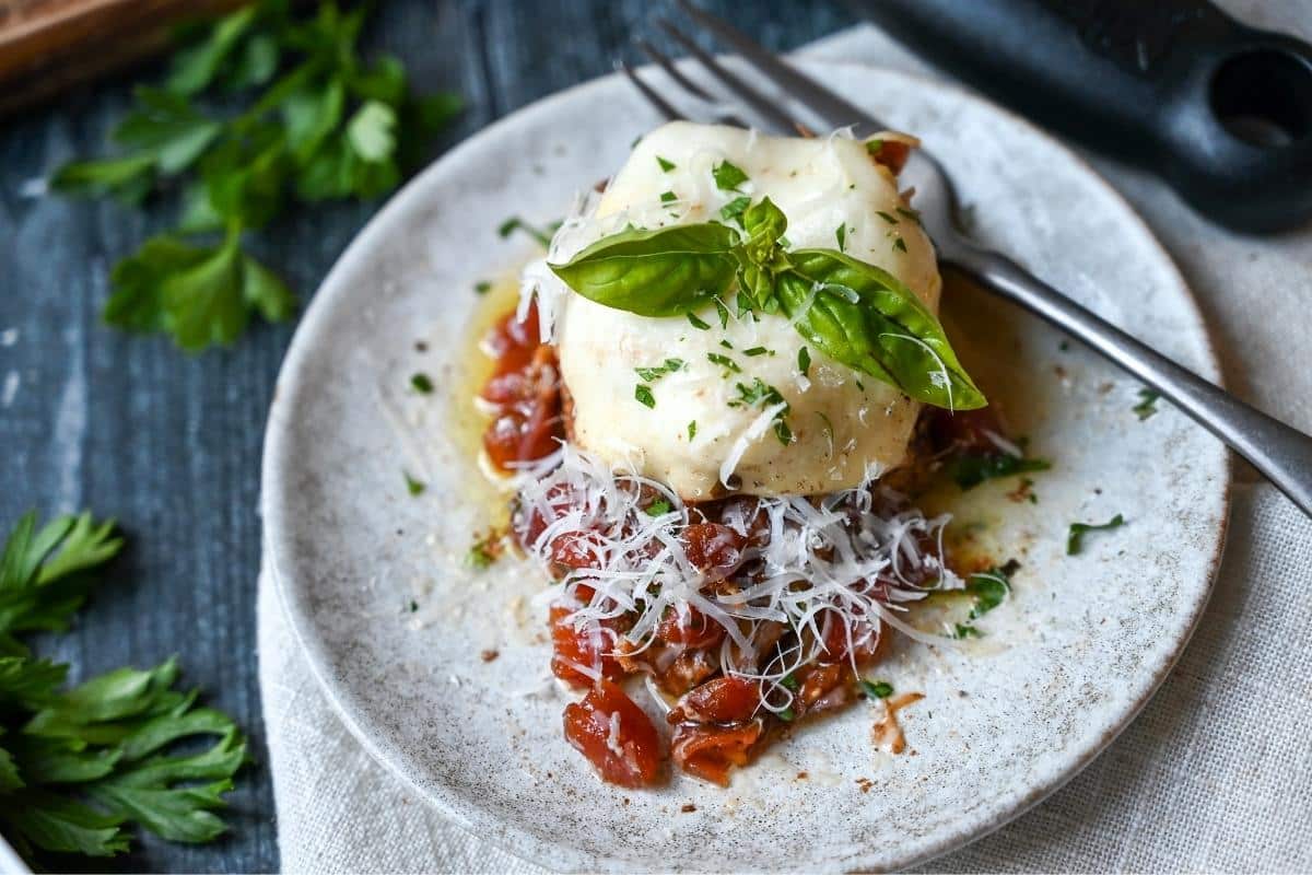 caprese chicken on a plate with fresh parm on top