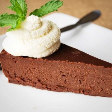 slice of dense chocolate cake on a white plate with a whipped cream and mint garnish