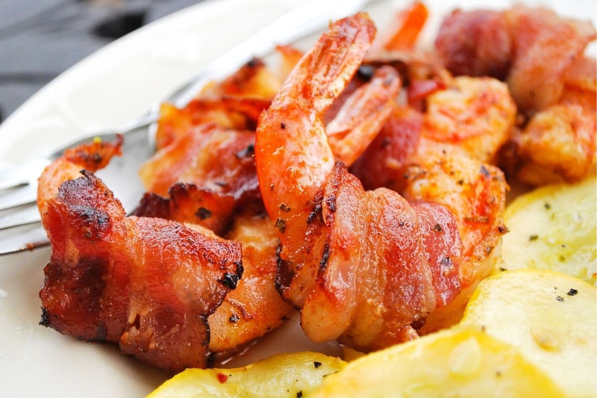close up of smoked shrimp wrapped in bacon with squash on a plate