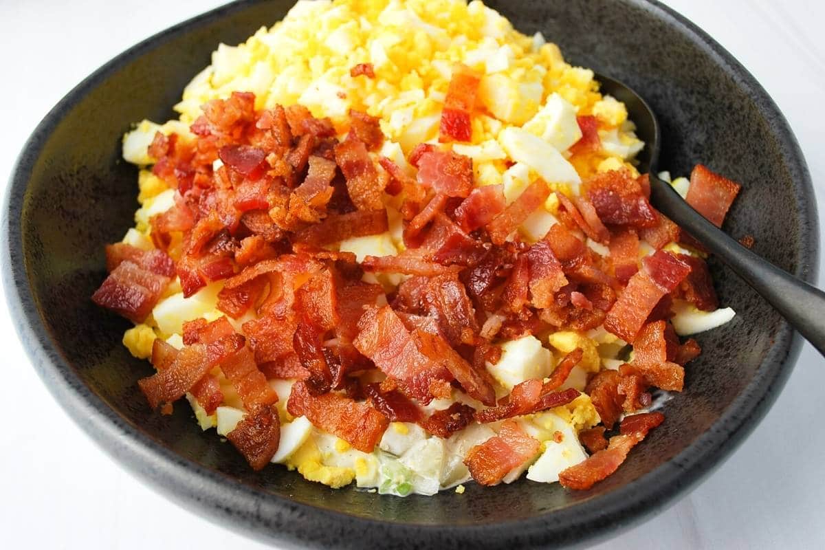 eggs and bacon mixed with egg salad dressing in a black bowl