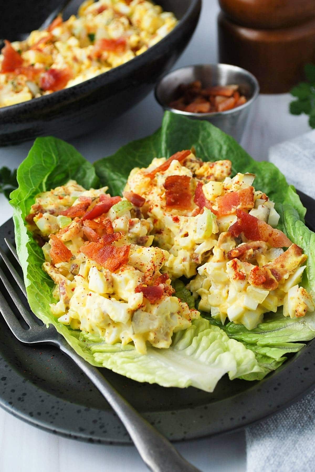 whole30 egg salad on top of romaine cups with crumbled bacon on top on a plate with a fork