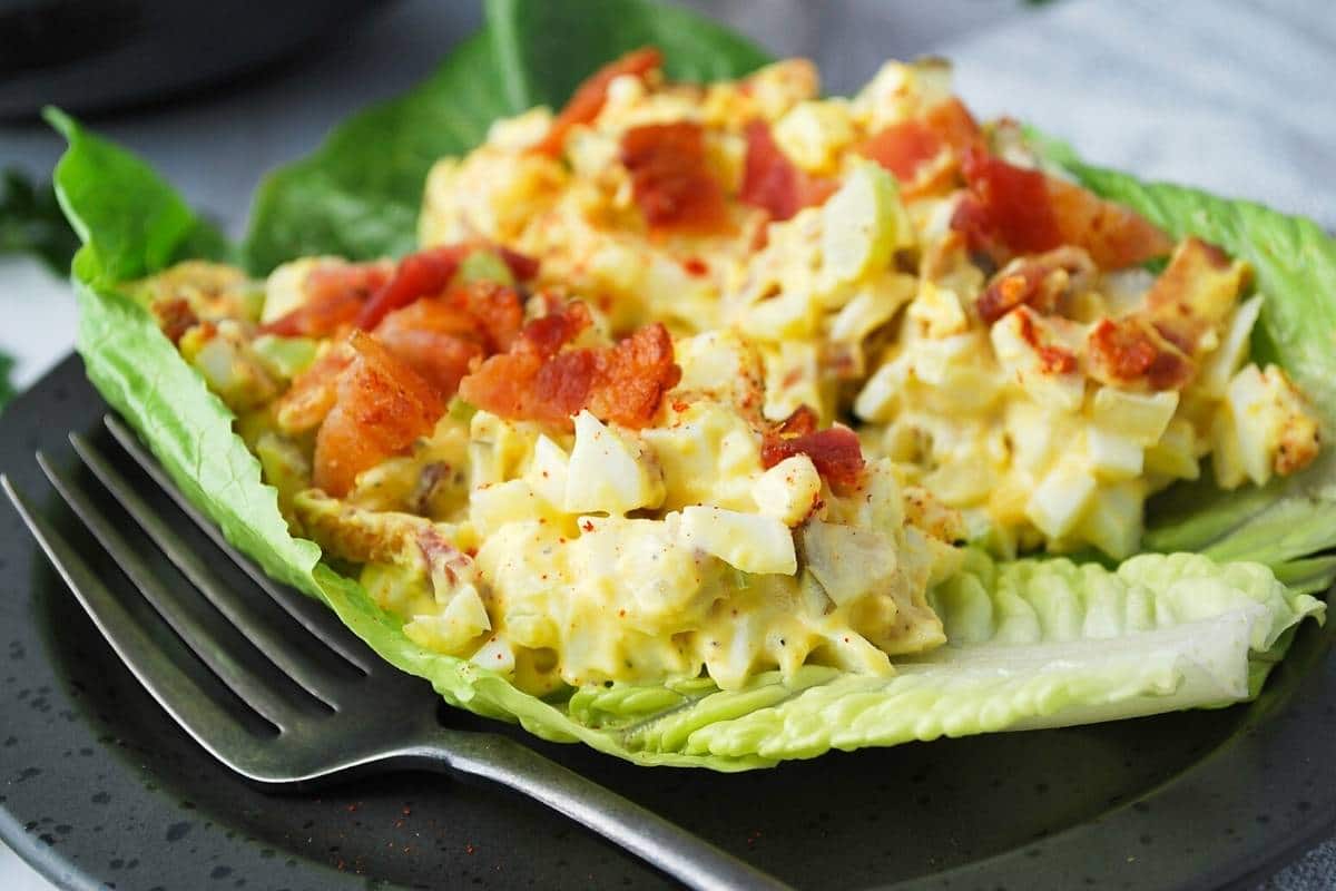 close up photo of two lettuce cups topped with egg salad and bacon with a fork