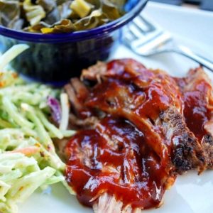 close-up photo of pulled pork barbecue on a plate with slaw and collard greens