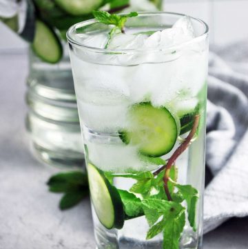 cucumber mint water in a glass with ice and a pitcher of infused water in the background