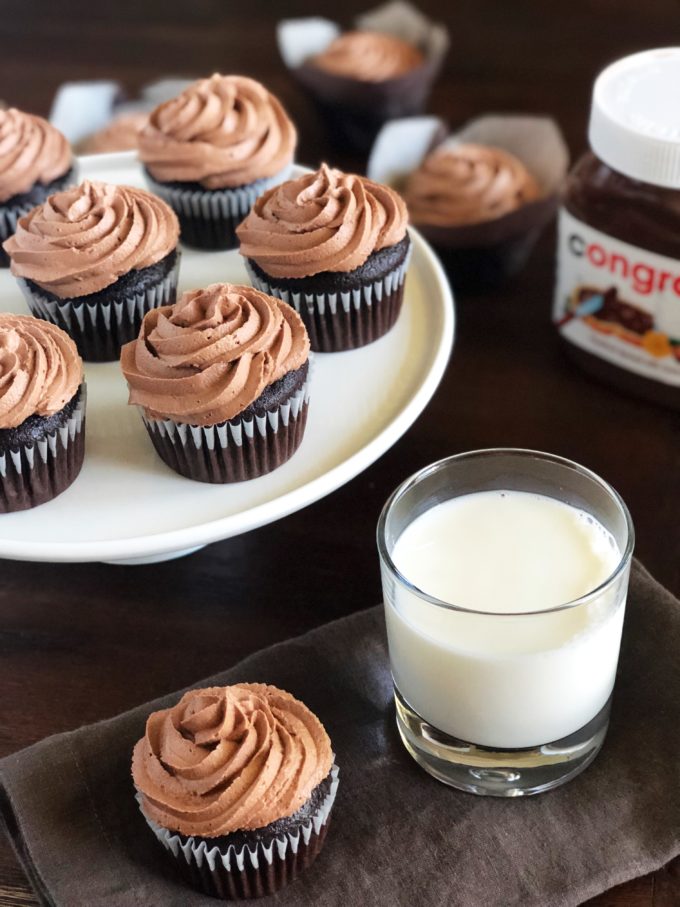 A cupcake with a glass of milk with platter of cupcakes in the background